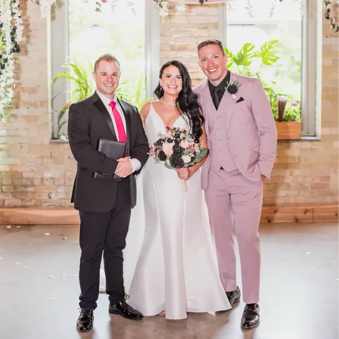 Wedding officiant Schwa Potter with newlyweds under floral garland at Milwaukee brick venue