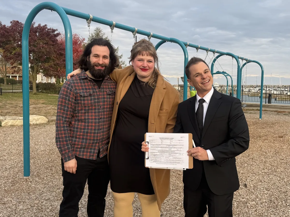 Couple holding signed marriage license with officiant Schwa Potter at a playground in Milwaukee